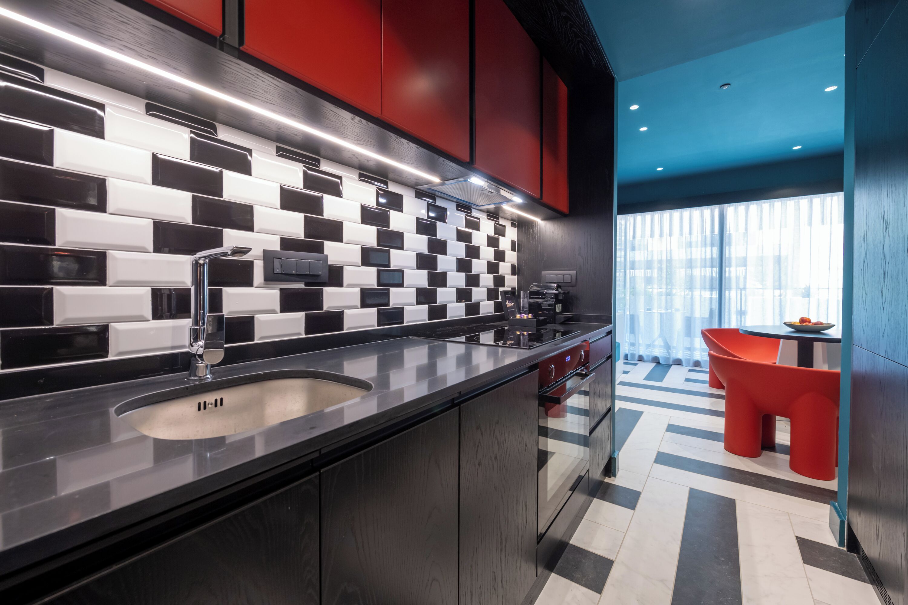 A modern kitchen with a black and white checkered backsplash, red cabinets, and a stainless steel sink.