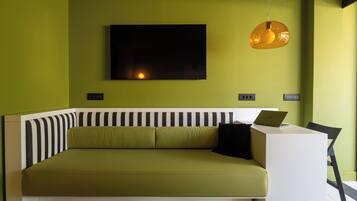 Quarto moderno com sofá verde, escrivaninha branca e cabeceira listrada em preto e branco.