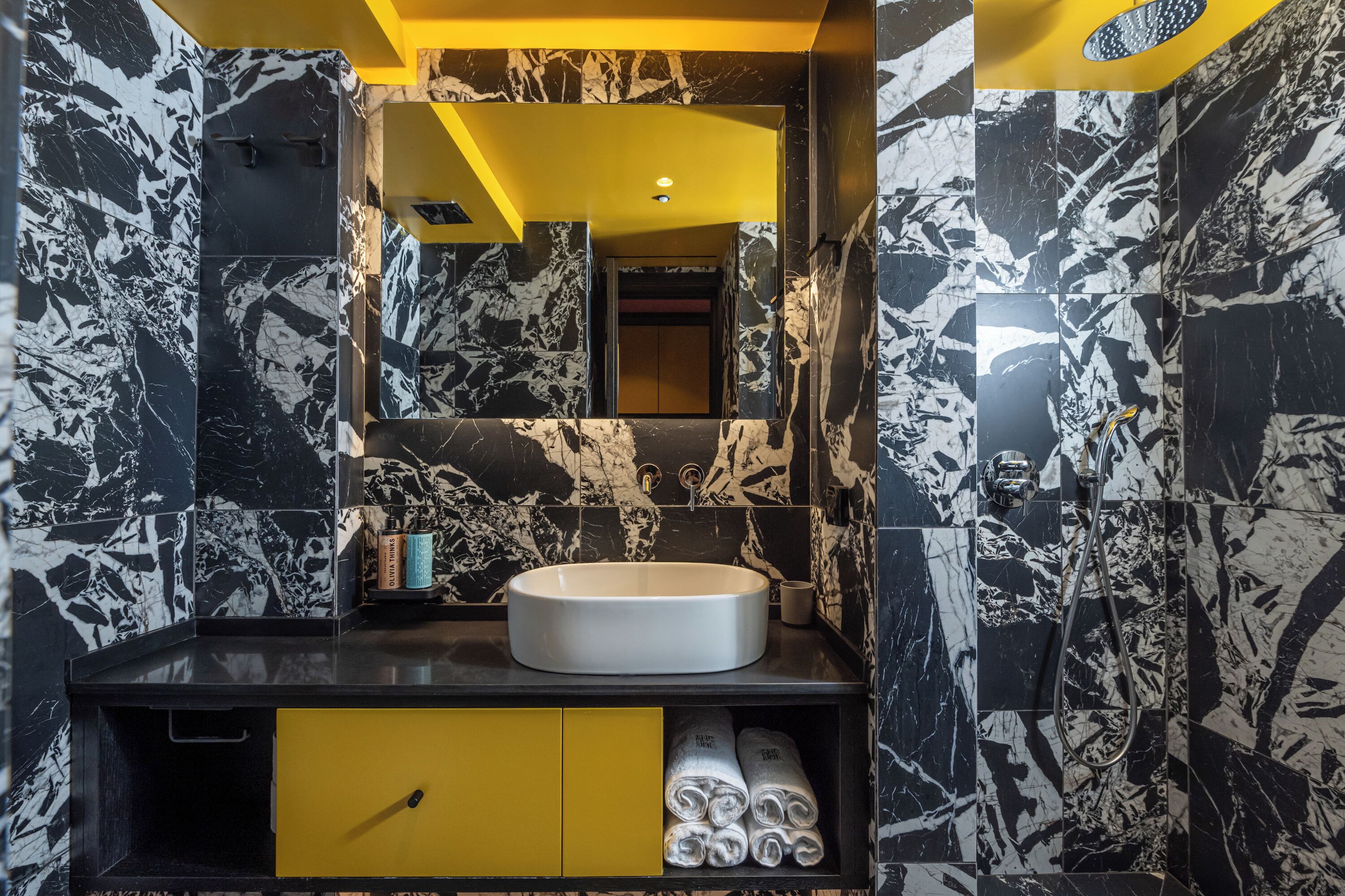 A bathroom with a black and white marble backsplash, a yellow vanity with a sink, and a mirror above it.