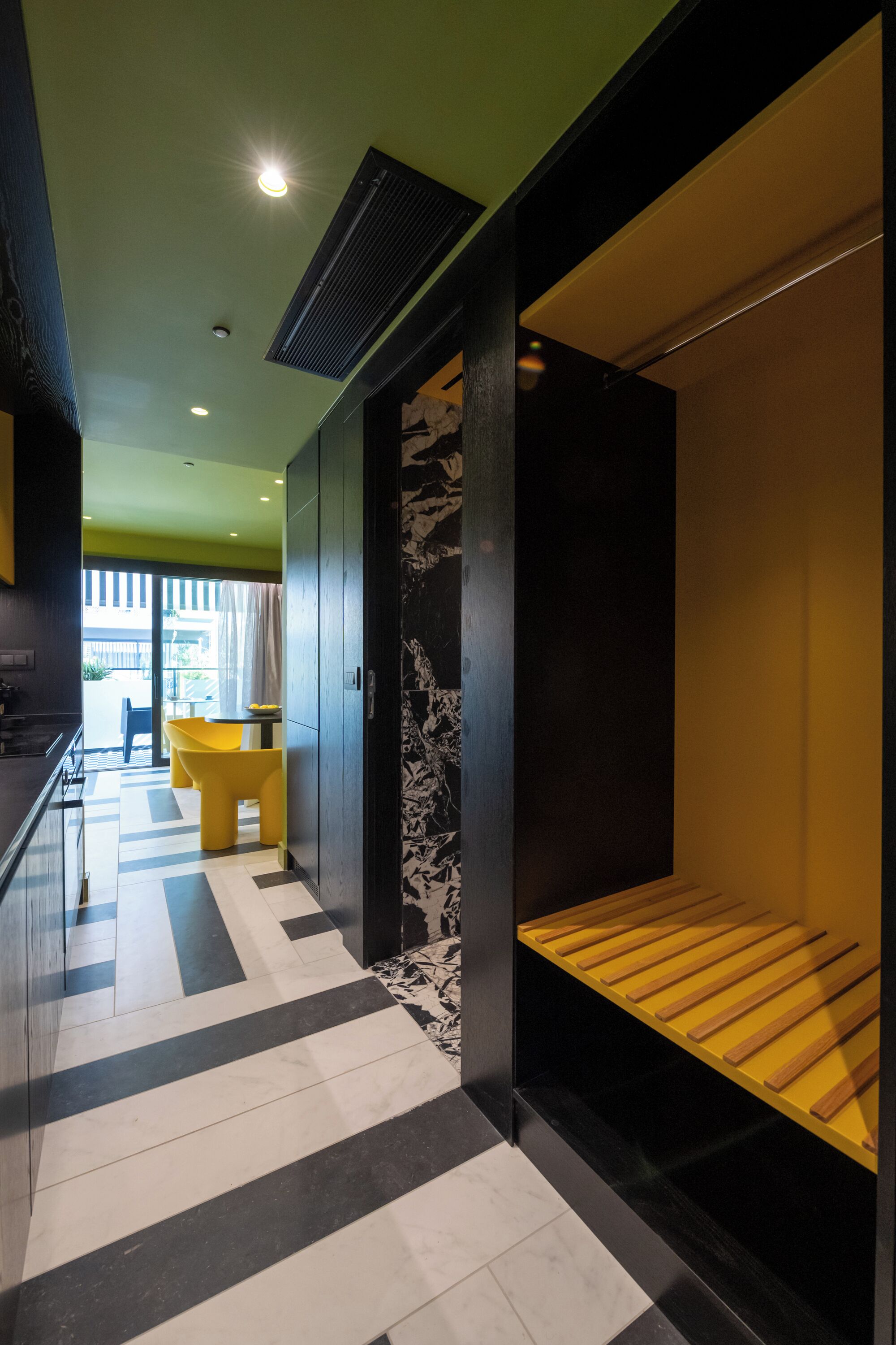 A modern interior with a black and white striped floor, a yellow bench, and a view of the outside.