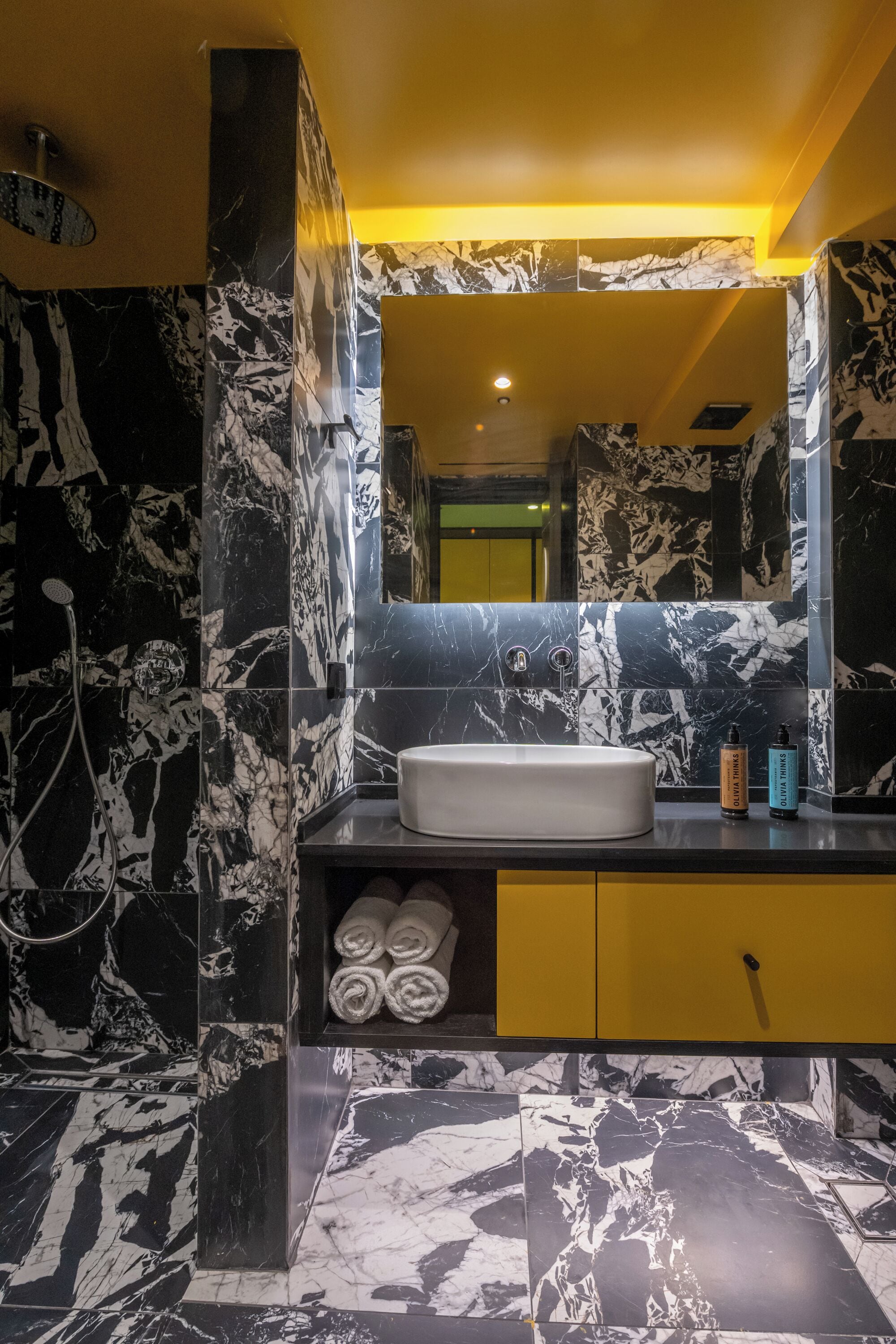 A bathroom with a marble sink, yellow cabinet, and a mirror reflecting the room.