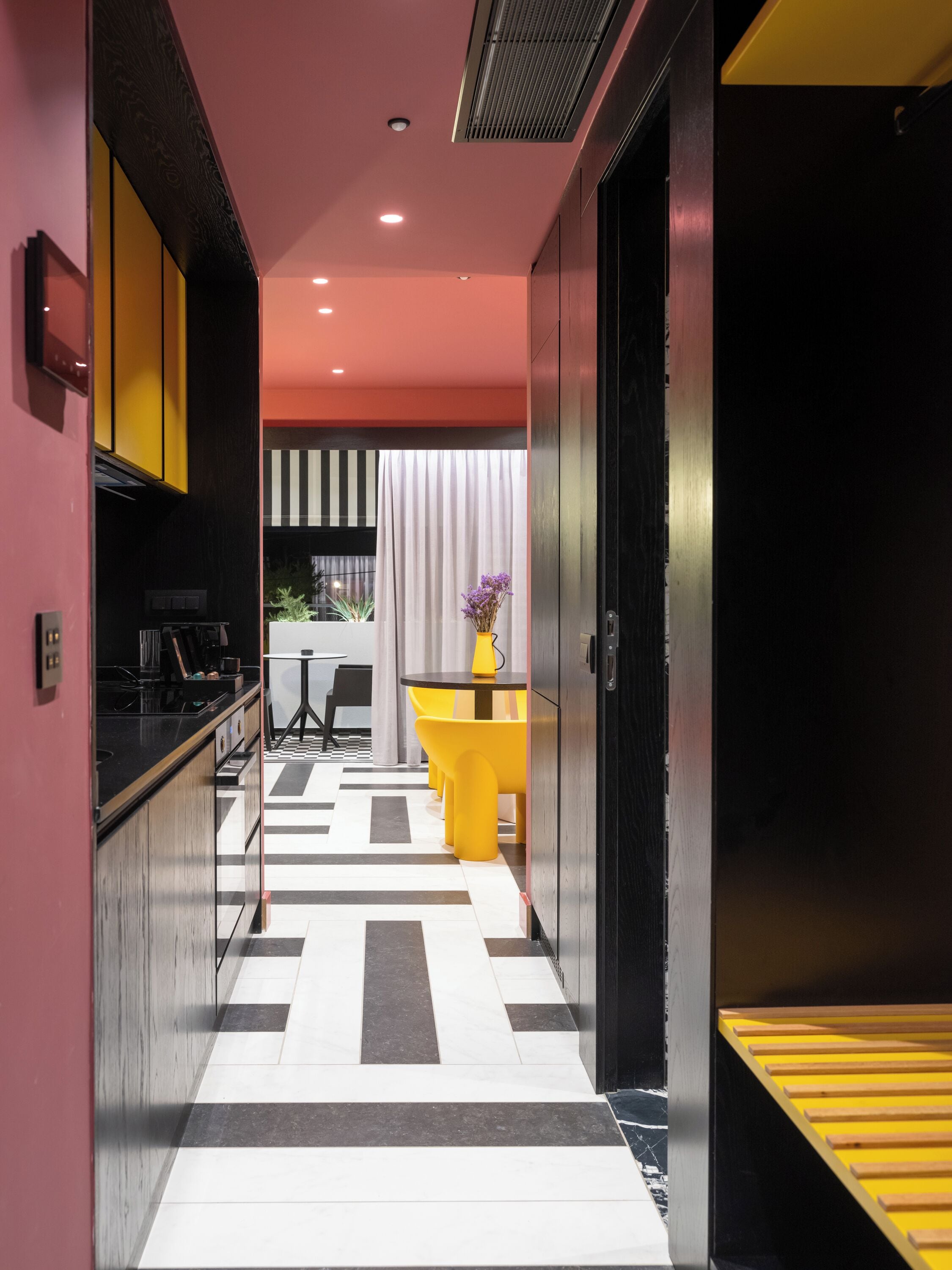 Una cocina moderna con encimera negra, una silla amarilla y una mesa con un jarrón de flores.