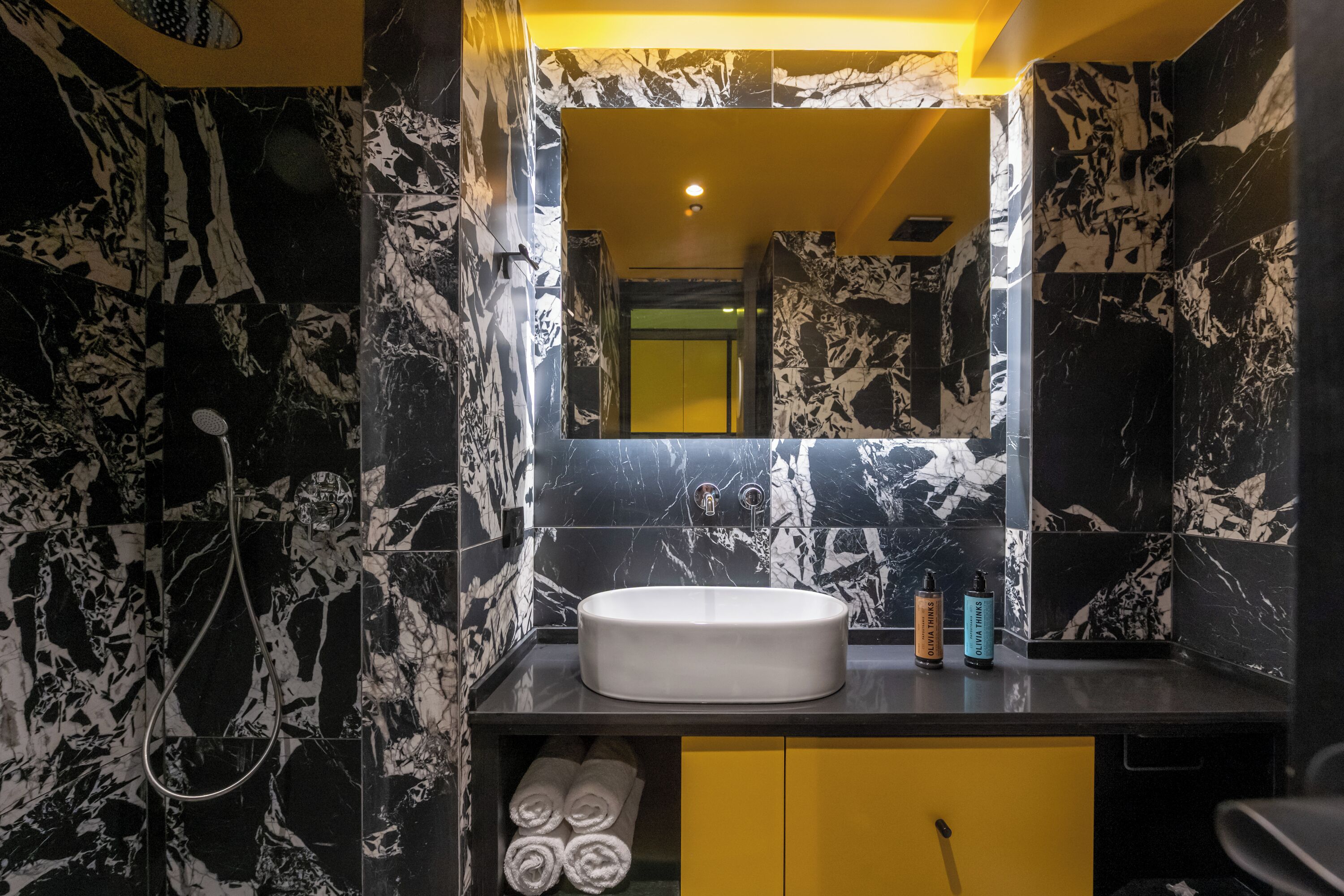Een badkamer met een marmeren wastafel, gele kastjes en een spiegel die de ruimte weerspiegelt.