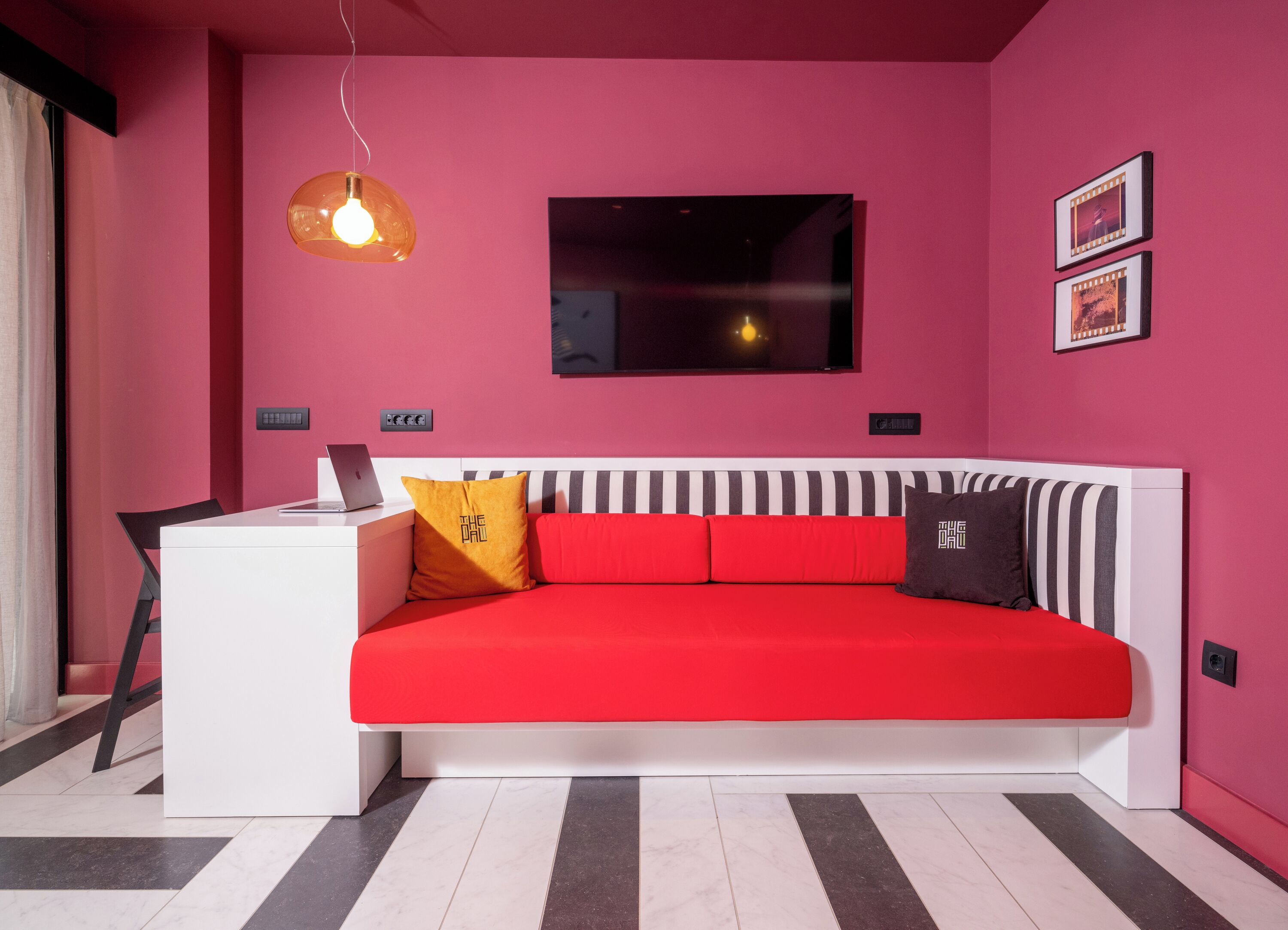 Una habitación moderna con un sofá rojo, un escritorio blanco y un cabecero a rayas negras y blancas.