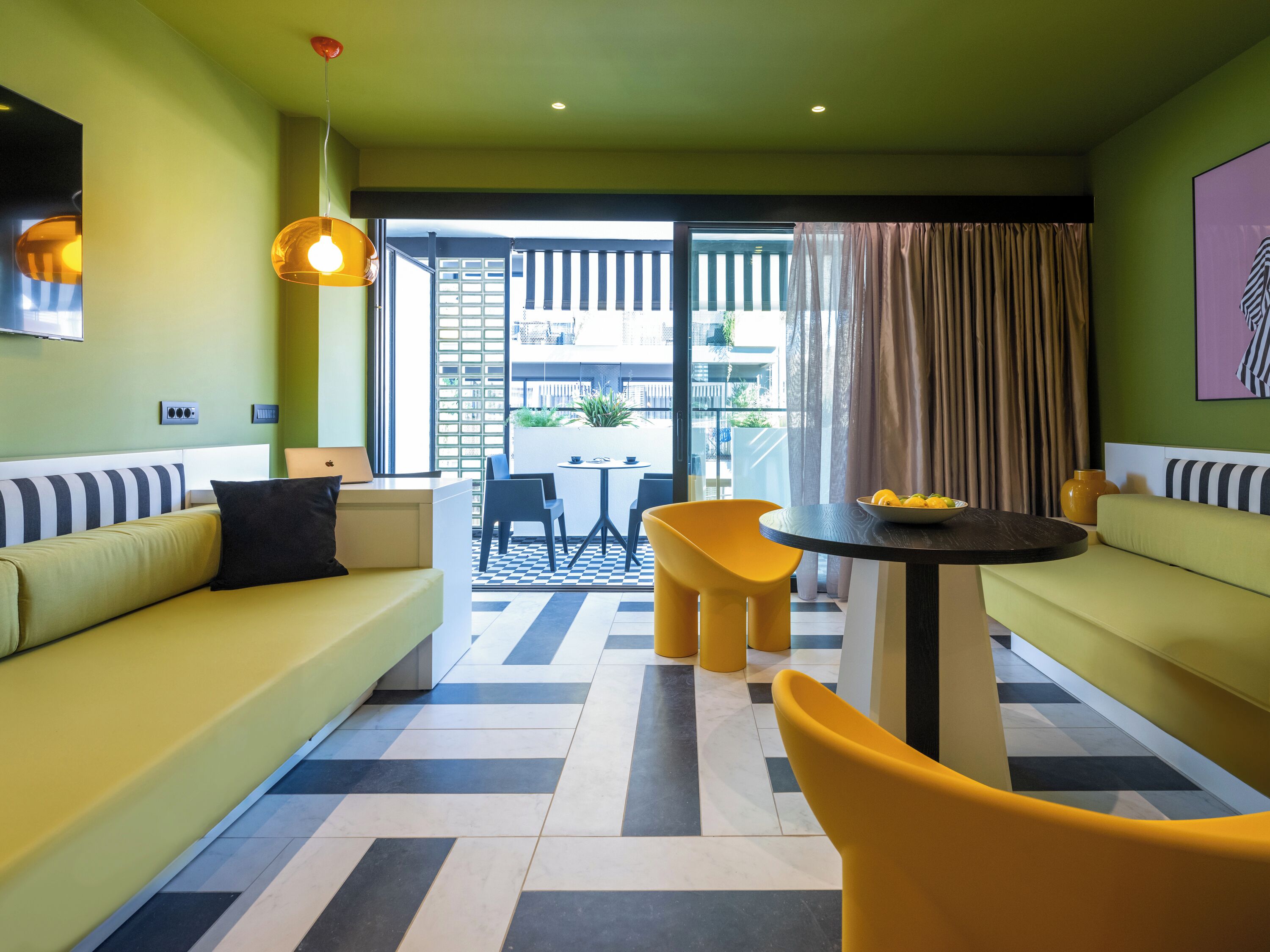 Una habitación de hotel moderna con sofá, sillas amarillas, una mesita y un balcón con vistas.
