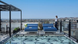A rooftop terrace with two blue lounge chairs, a small table, and a glass balustrade overlooking a cityscape. - The Pal Living in a Concept (Heraklion)