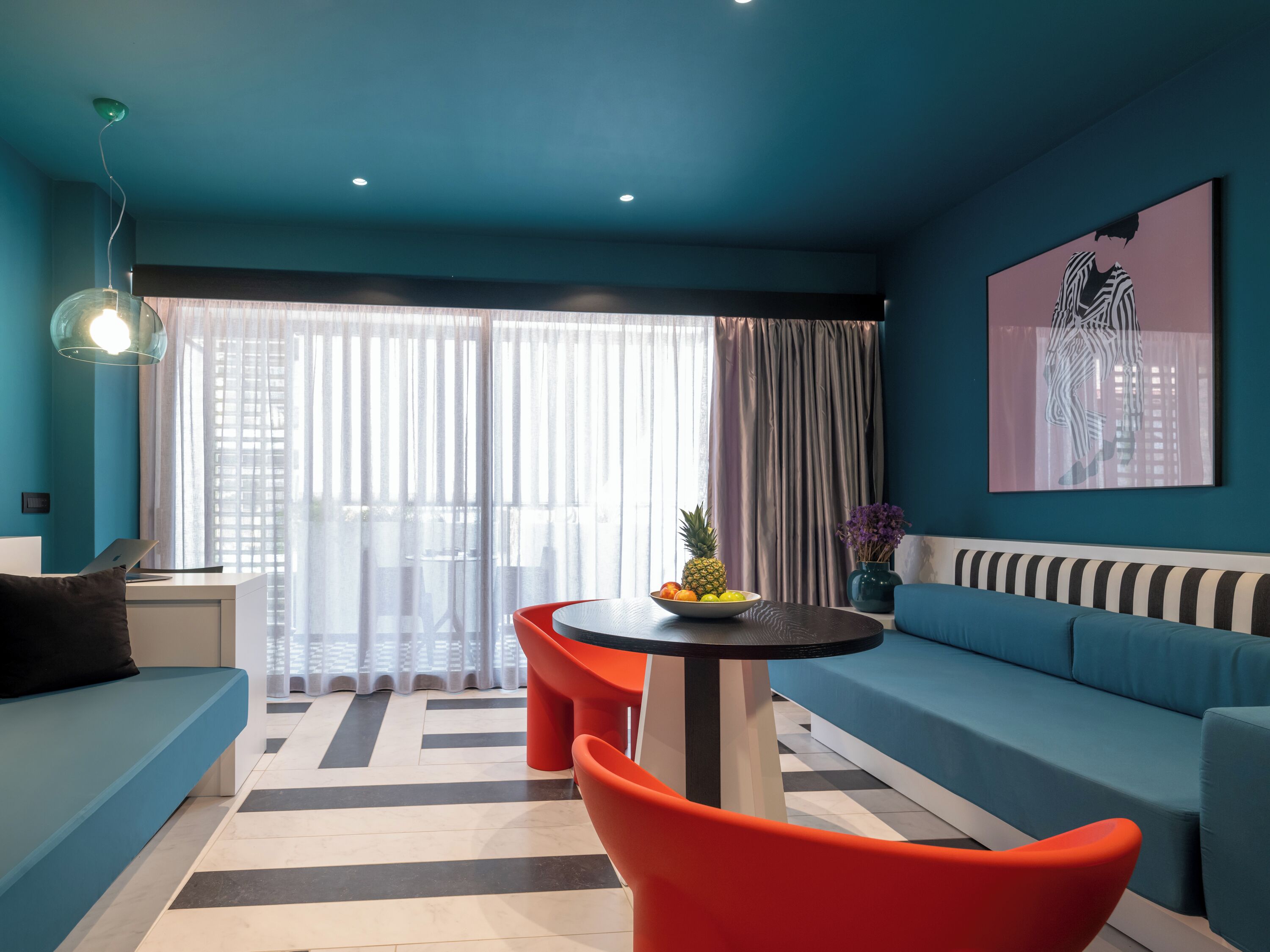 A modern living room with a blue sofa, a round table with a fruit bowl, and a red chair.