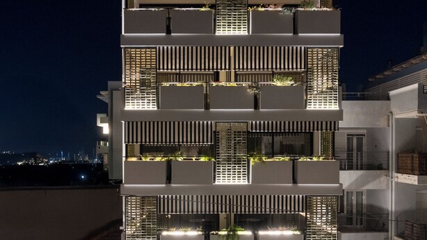 A multi-story building with balconies, a ground-level entrance, and a view of the cityscape in the background. - The Pal Living in a Concept (Heraklion)