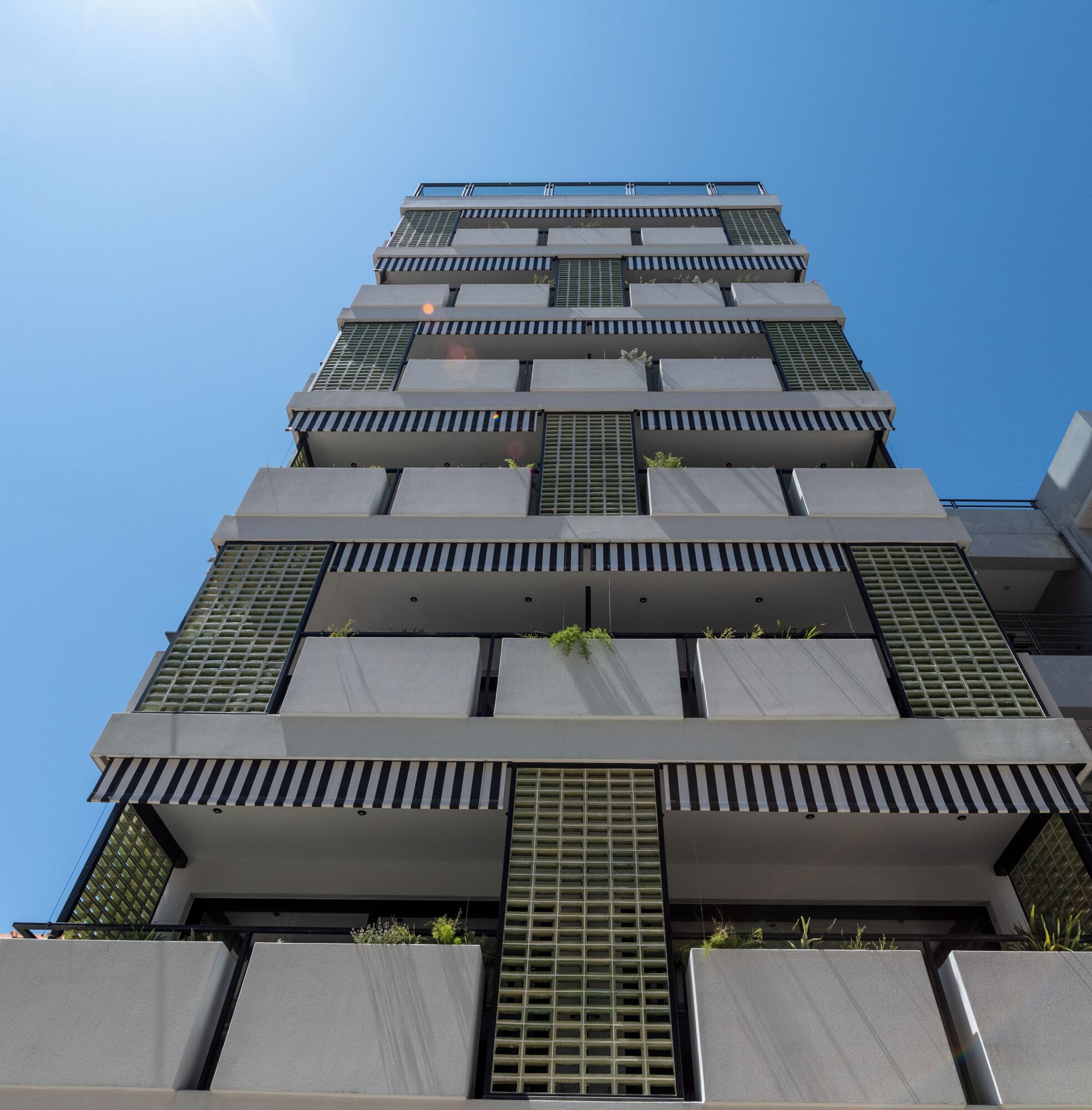 A modern high-rise building with multiple balconies and a clear sky.