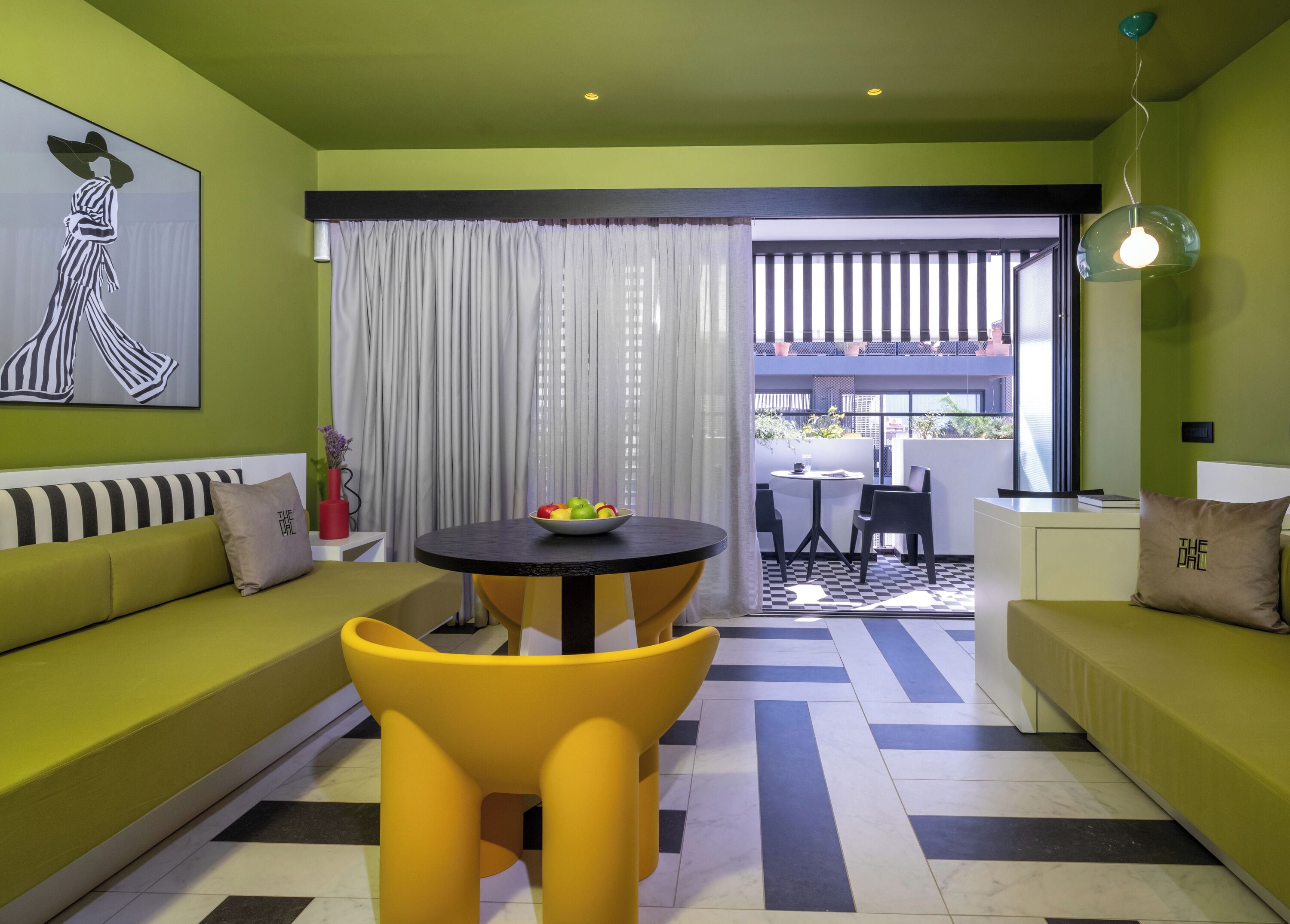 Ein modernes Wohnzimmer mit einer Couch, gelben Sesseln, einem Esstisch mit Obstschale und Blick auf einen Balkon.