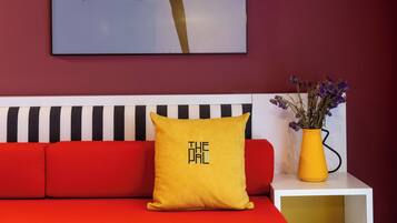 A modern living room with a red sofa, a yellow pillow with text, a black and white striped cushion, a vase with flowers, and a framed artwork on the wall.