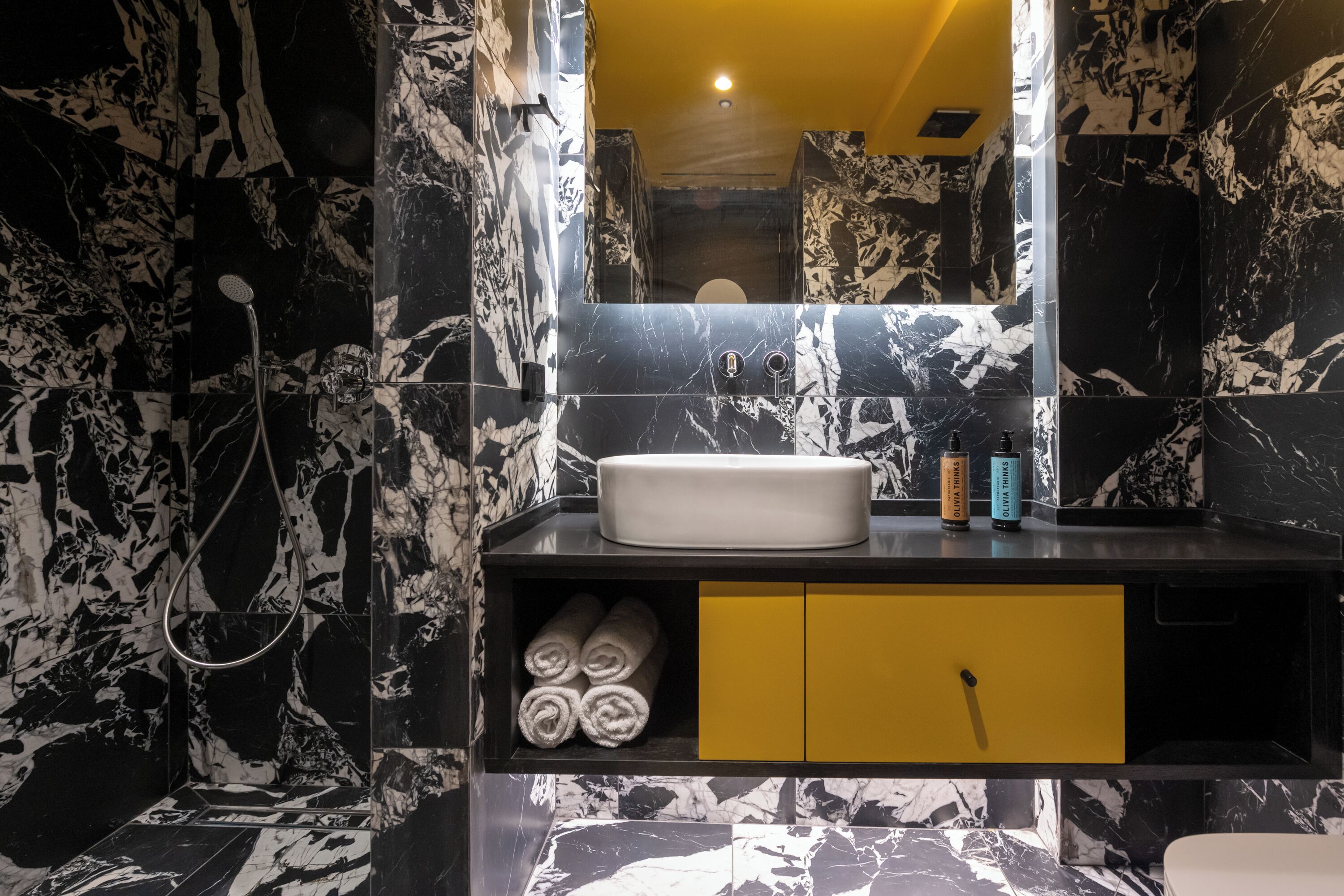 Casa de banho com painel de bancada em mármore preto e branco, um armário amarelo e uma pia branca.