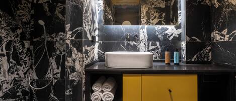 Casa de banho com painel de bancada em mármore preto e branco, um armário amarelo e uma pia branca.