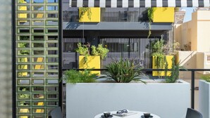 A modern outdoor seating area with a checkered floor, black chairs, a round table, and yellow planters with greenery. - The Pal Living in a Concept (Heraklion)