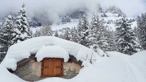 A snow-covered mountain hut with a wooden door, surrounded by snow-laden trees and a misty mountain backdrop. - 6-person apartment (PASSY)