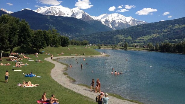 A lakeside view with people sunbathing and swimming, surrounded by mountains and greenery. - 6-person apartment (PASSY)
