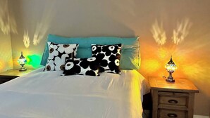 Una cama con ropa de cama blanca, almohadas color turquesa y almohadas estampadas en blanco y negro. Hay dos mesitas de noche con lámparas, una a cada lado de la cama.