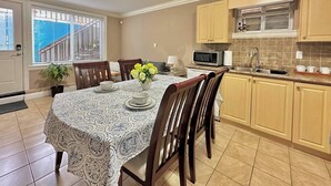 Un comedor con una mesa dispuesta para cuatro personas, un microondas y un lavamanos en la cocina contigua.