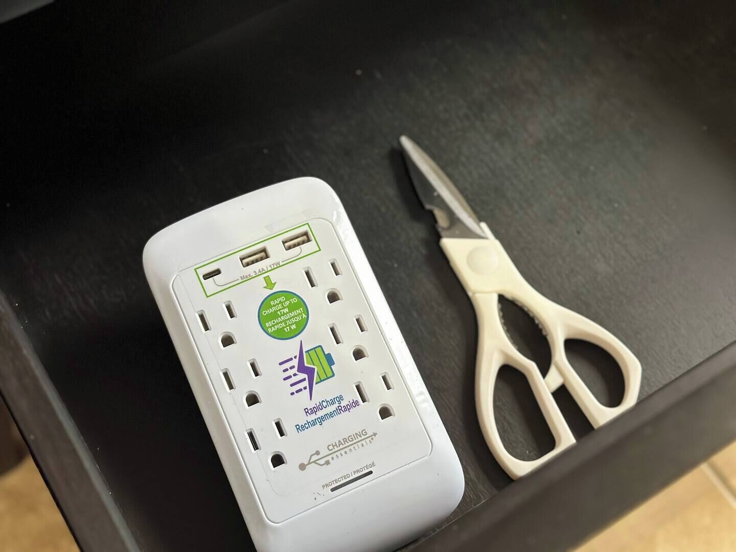 Un dispositivo RapidCharge RechargingRapidCharge blanco con puertos USB y un par de tijeras color beige sobre una superficie negra.