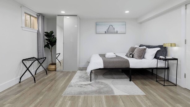 A modern bedroom with a bed, bedside table, and a large window. - Cozy Basement suite Near UBC, Kits, and DT (Vancouver)