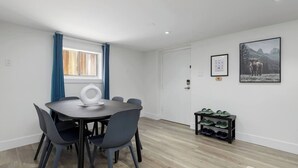 A modern dining area with a round table and chairs, a window with curtains, and a shoe rack with multiple pairs of shoes. - Cozy Basement suite Near UBC, Kits, and DT (Vancouver)
