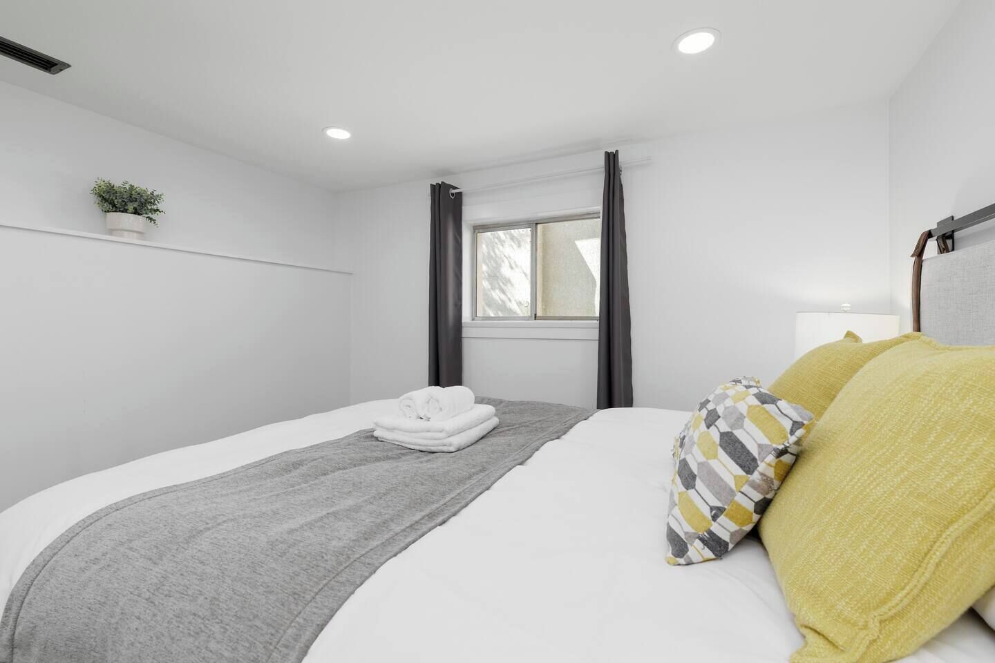 A modern bedroom with a neatly made bed, a grey throw blanket, and a potted plant on the wall.