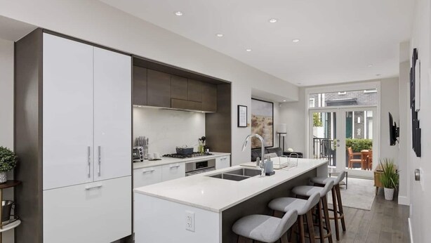 A modern kitchen with white cabinetry, a central island with stools, and a view to an outdoor patio.