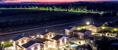 A residential area with multiple houses, each with a swimming pool and well-lit surroundings.