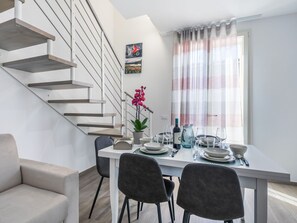 A modern dining area with a staircase, a dining table set for four, and a potted orchid.