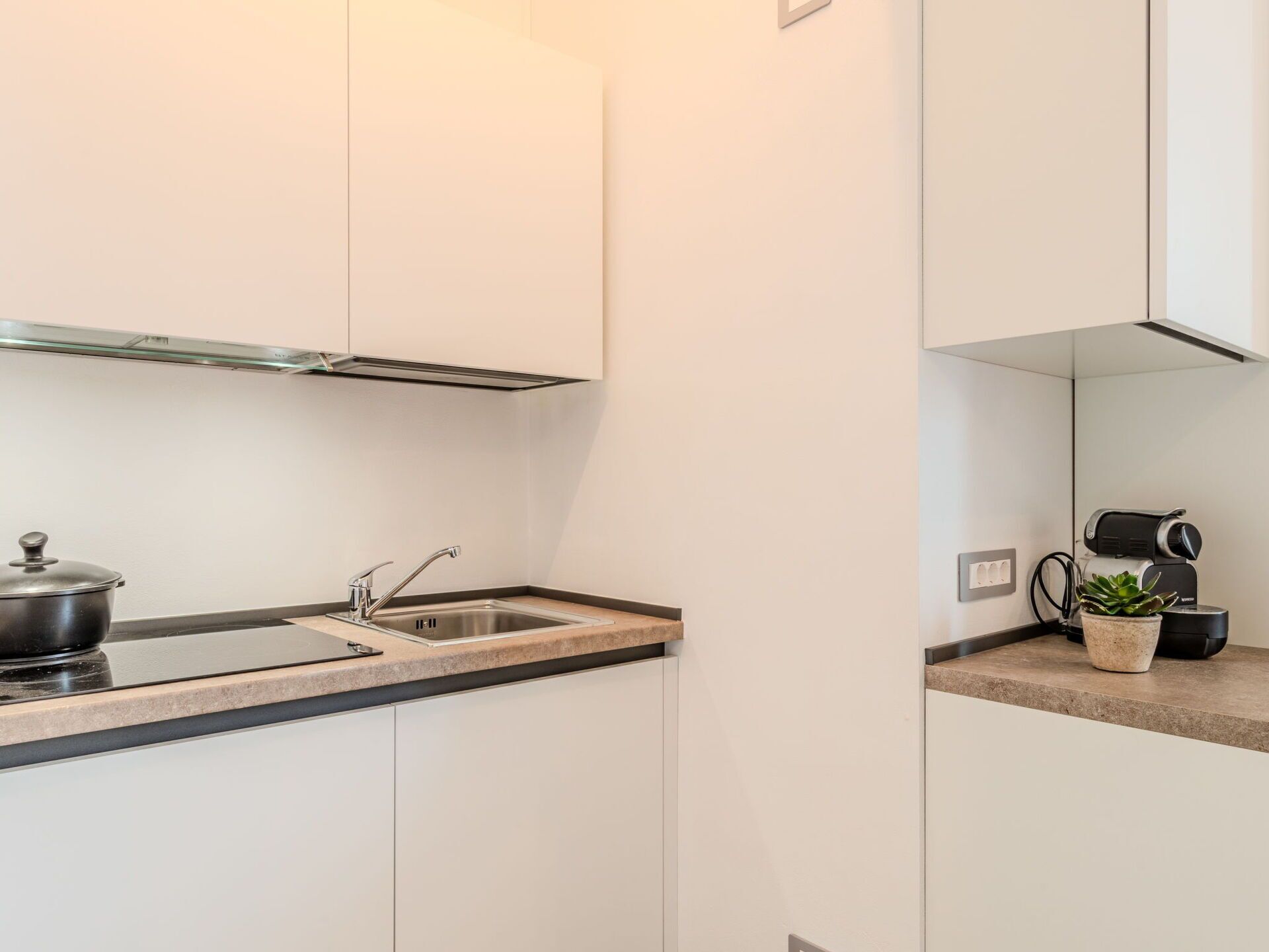 Une cuisine moderne avec des meubles blancs, un évier en acier inoxydable et une casserole noire sur la cuisinière.