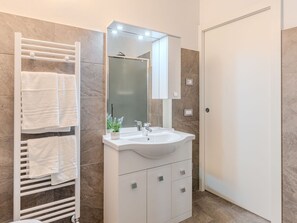 Une salle de bain moderne avec un meuble-lavabo blanc, une cabine de douche en verre et un porte-serviettes muni de plusieurs serviettes.