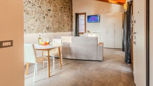 Ein gemütliches Interieur mit einer Steinwand, einer Holzbalkendecke, einer Essecke mit Tisch und Stühlen, einer Couch und einem an der Wand befestigten Fernseher.