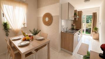 A modern kitchen with a dining area, featuring a wooden table set for a meal, a round woven wall decoration, and a view of the outdoors.