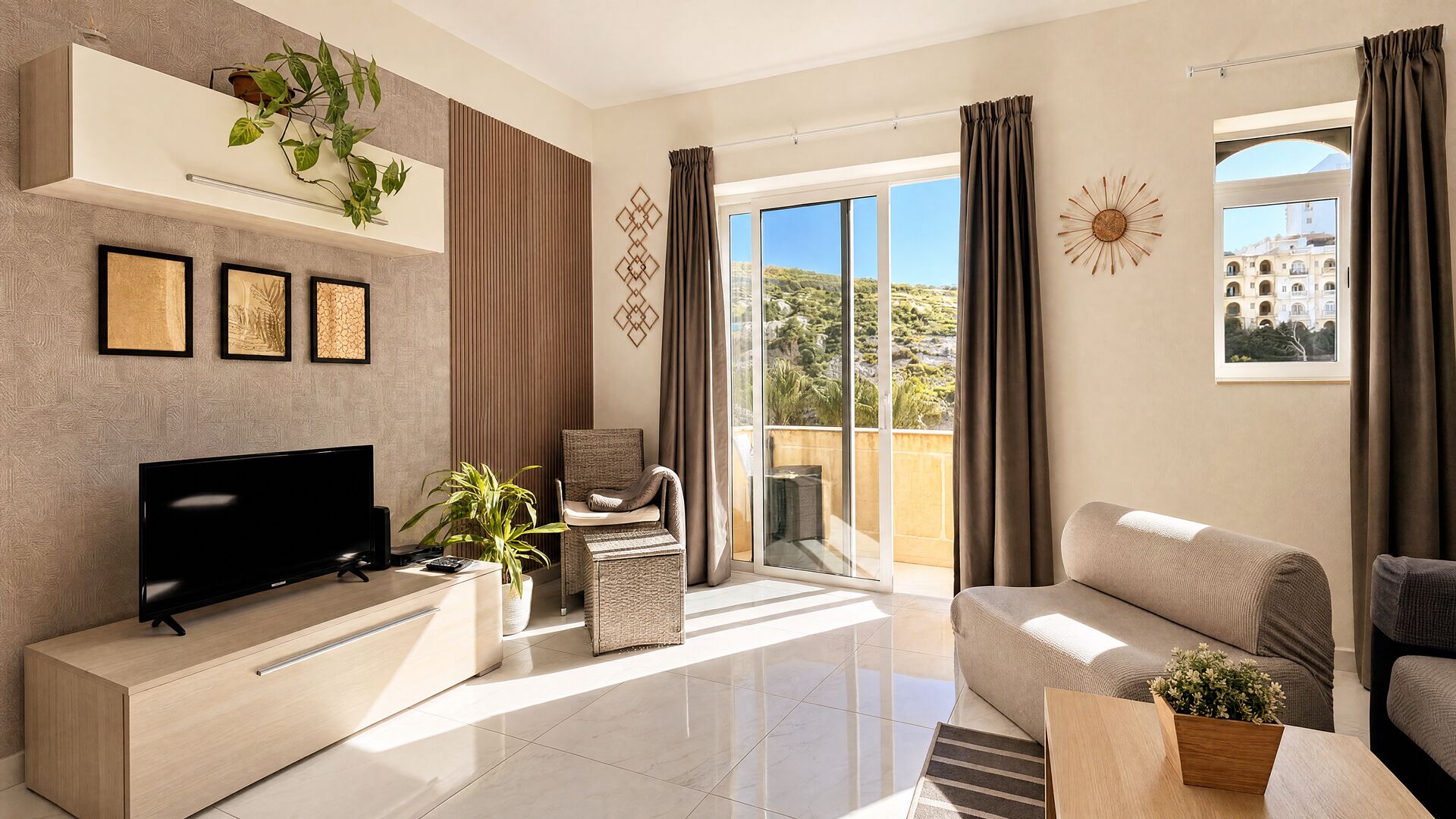 Una sala de estar moderna con televisor de pantalla plana, un sofá, una silla y un balcón con vistas a vegetación y un edificio.
