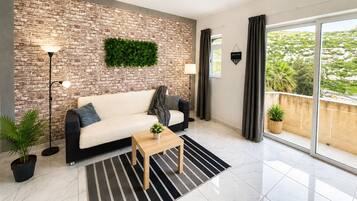 Uma sala de estar moderna com parede de tijolos, um sofá, uma mesa de centro e vista através de uma porta de vidro deslizante.