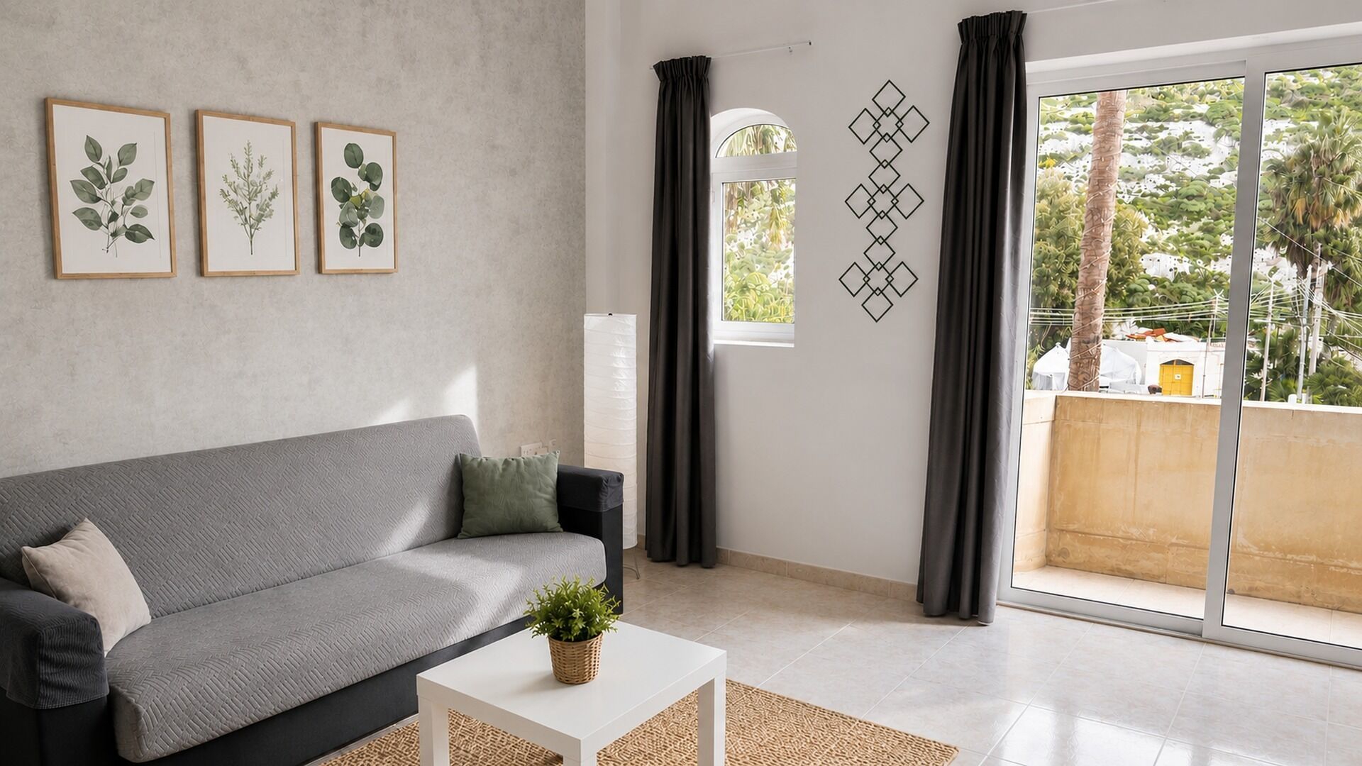 Un soggiorno moderno con un divano grigio, un tavolino da caffè bianco e una pianta in vaso. Alle pareti, tre stampe botaniche incorniciate e un decoro geometrico.
