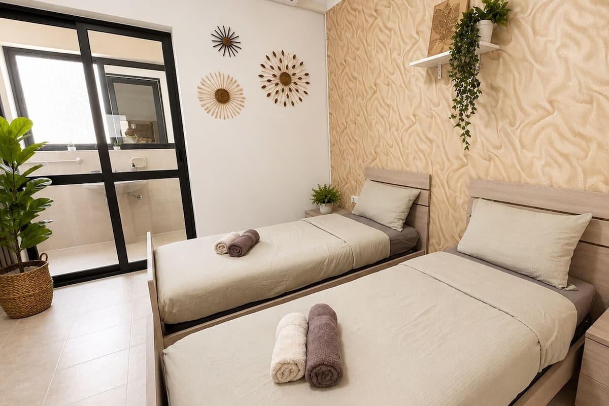 A hotel room with two beds, a bathroom with a large mirror, decorative wall art, and potted plants.
