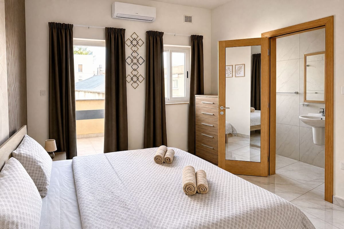 A hotel room with a bed, a dresser, a mirror, and an air conditioning unit.