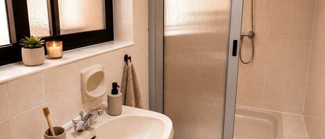 Ein Badezimmer mit Waschbecken, Spiegel, Fenster mit Milchglas, Dusche und Handtuchhalter.