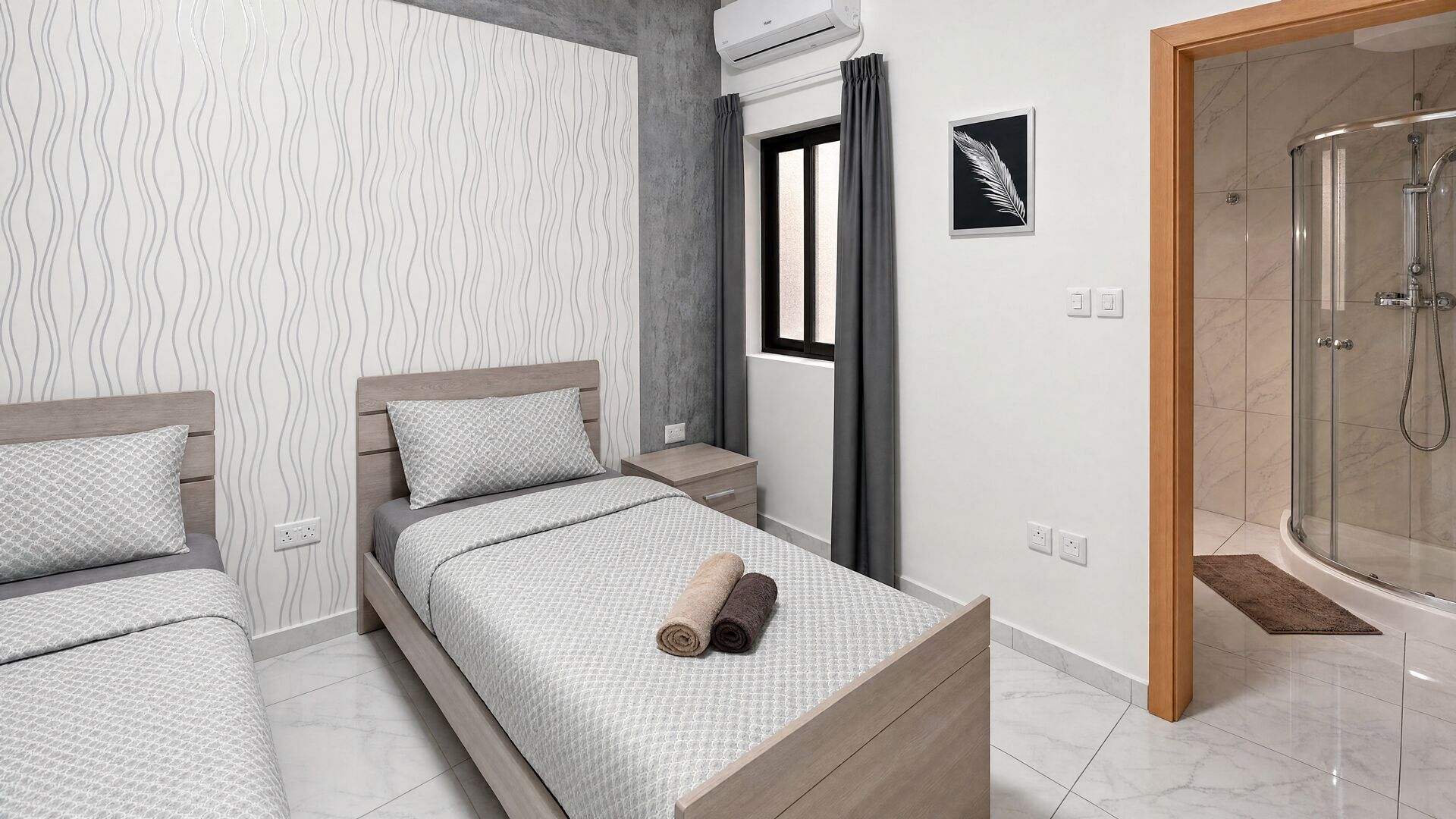 A modern bedroom with a bed, a nightstand, a window with curtains, an air conditioning unit, a framed picture, and a shower area.