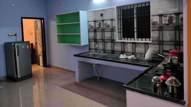 A kitchen with a black countertop, a sink, a refrigerator, and a window with decorative tiles. - 1BHK Spacious stay near Ramana Ashram in Tiruvannamalai (Tiruvannamalai)
