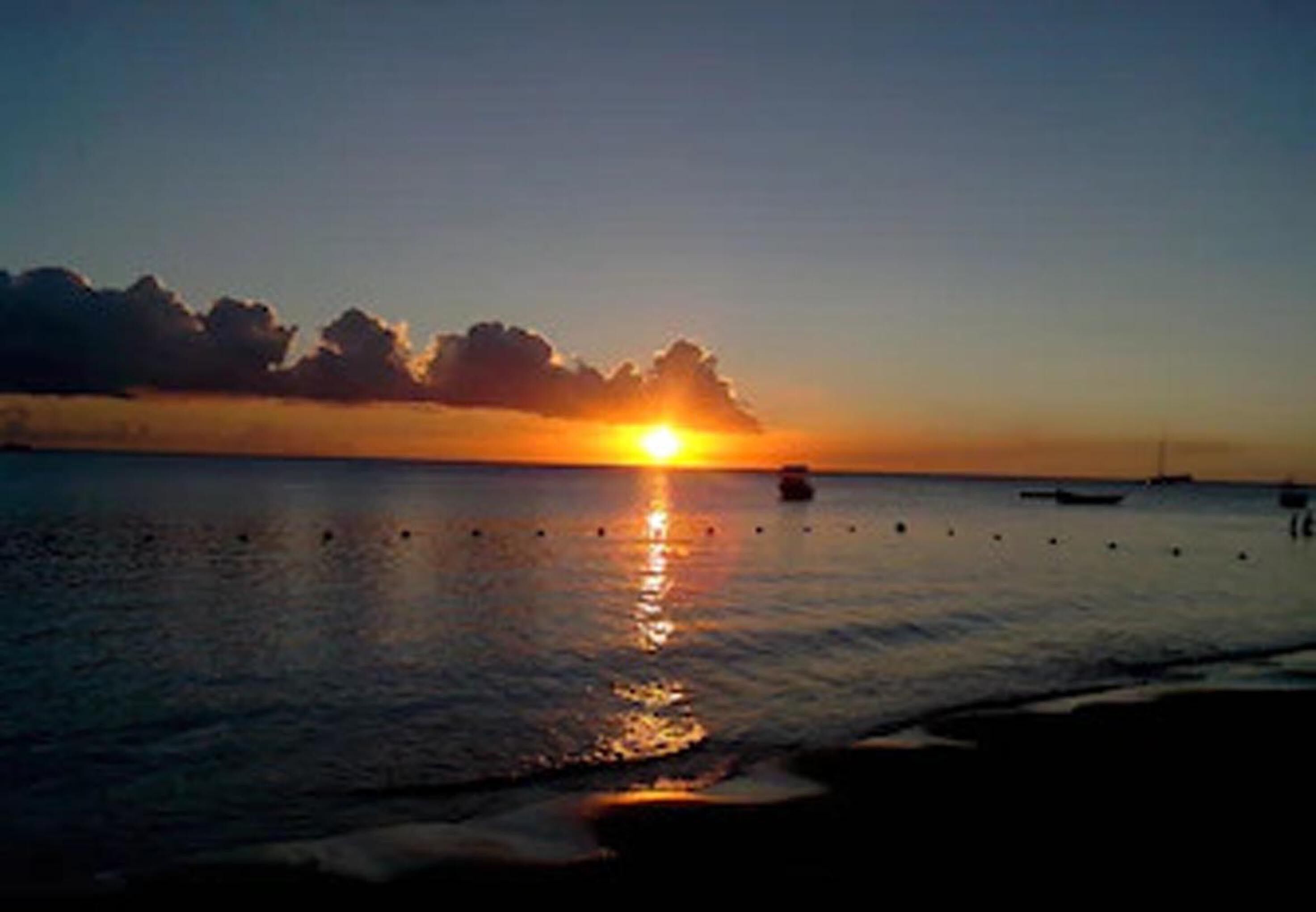 Un coucher de soleil sur une mer calme, avec des bateaux et des bouées.