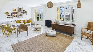 Ein heller, geräumiger Wohnraum mit hoher Decke, großen Fenstern und einer gemütlichen Sitzecke mit Sofa und Sesseln.