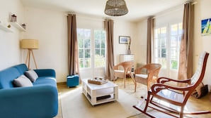 A living room with a blue sofa, a wooden rocking chair, a white coffee table, and wicker furniture. - House for 7 people 900m from the beach (Barbâtre)