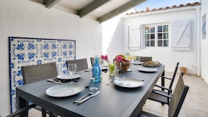 A dining table set for two with plates, cutlery, and glasses, a vase with flowers, and a basket of bread. - House for 7 people 900m from the beach (Barbâtre)
