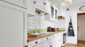 A kitchen with white cabinets, a wooden countertop, a coffee machine, and a hanging apron. - House for 7 people 900m from the beach (Barbâtre)