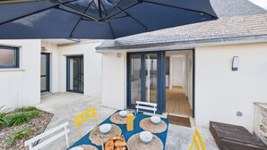 A patio with a table set for breakfast, including croissants and bowls, under a large umbrella.