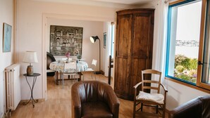 Habitació amb sòl de fusta, una cadira de cuir marró, un armari de fusta, una taula amb caires i una vista a través d'una finestra.