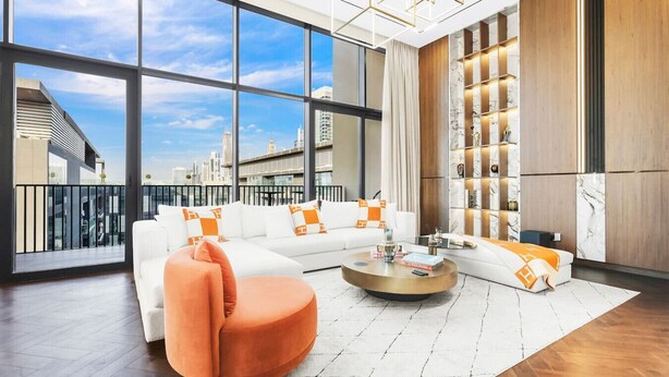 Un salon moderne avec un canapé d’angle blanc, une table basse ronde et une grande fenêtre donnant sur la ville.