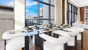 Un espace de salle à manger moderne avec une table en verre, des chaises blanches rembourrées et une vue sur la ville grâce à de grandes fenêtres.